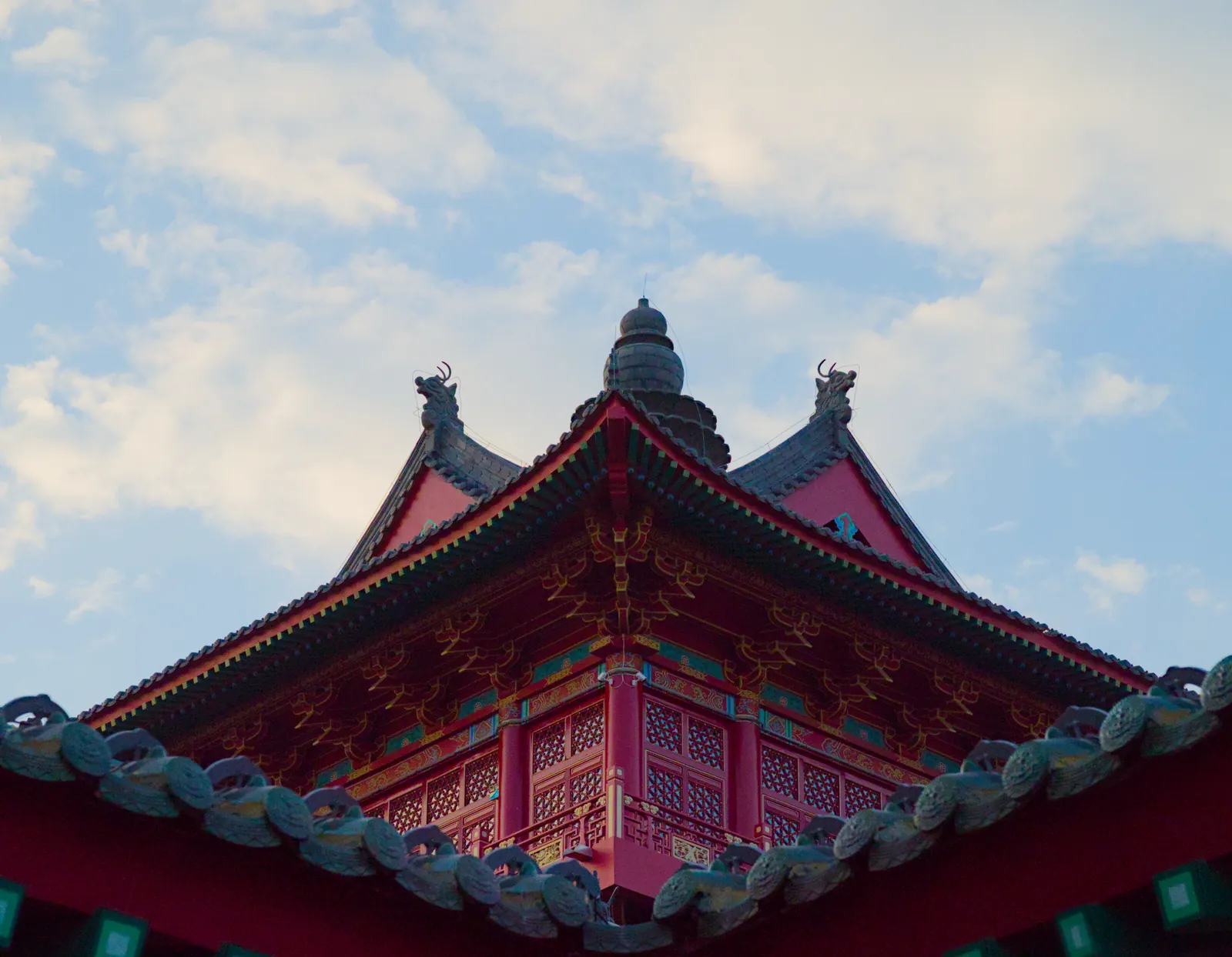 仰拍仿古建筑的攒尖屋顶：檐角起翘，顶部立着深色宝顶，垂脊两端为龙形吻兽，红墙上可见贴金斗拱与菱花格窗